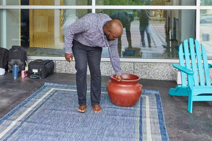 A person dragging a pot across the Unique Loom Outdoor Collection Transitional Indoor/Outdoor Area Rug