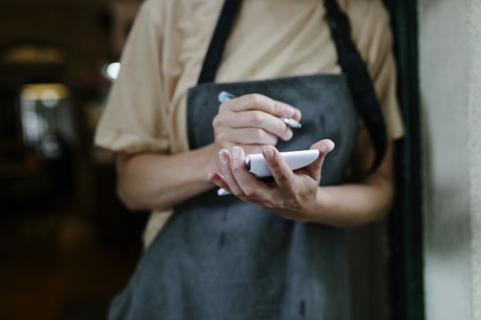 A waiter's hands and apron, holding a notepad and pen