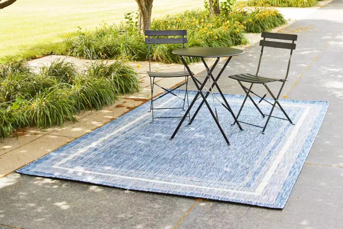 A pair of chairs and a table on the Unique Loom Outdoor Collection Transitional Indoor/Outdoor Area Rug placed on a concrete walkway