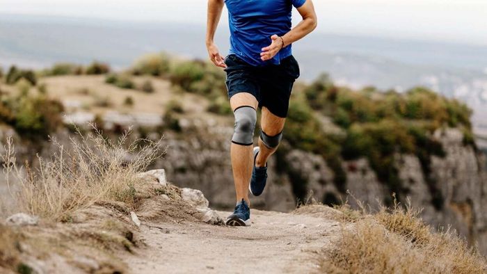 A runner with knee braces traversing a trail