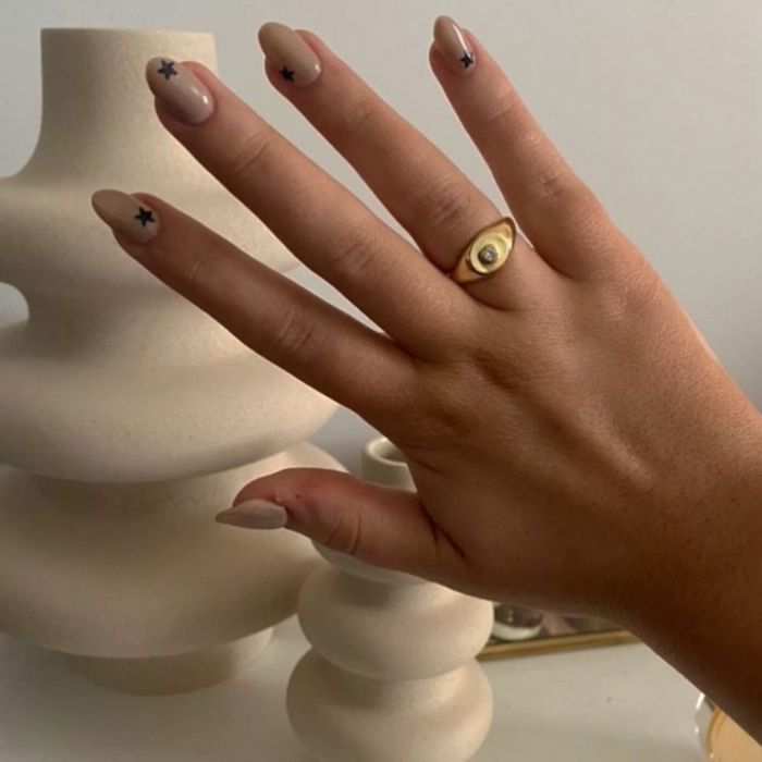 A subtle nude nail design accented with delicate black star details.