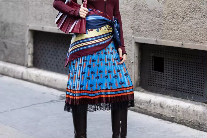 Violet Grace Atkinson showcases a chic autumn ensemble featuring a burgundy cardigan, a stylish bag, a wrapped scarf, a blue-laced black skirt, and boots at Lacoste during the Womenswear Spring/Summer 2025 show at Paris Fashion Week on October 01, 2024, in Paris, France.