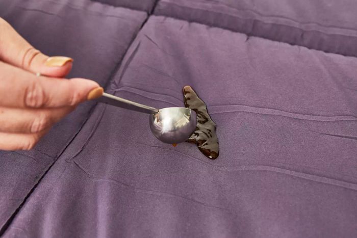 Hand pouring liquid onto a purple Utopia Bedding All-Season Down Alternative Comforter
