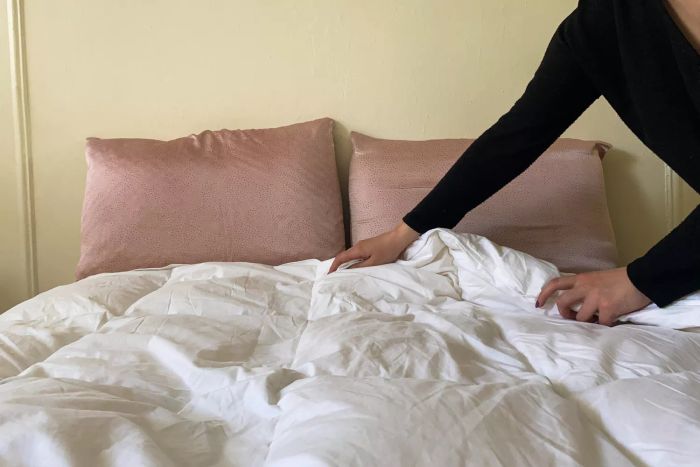 A person folding the Fluff Co Down Blended Comforter on a bed