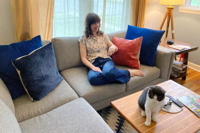 A person relaxing on the BenchMade Modern Skinny Fat Sectional in their living room, accompanied by a cat and a coffee table.