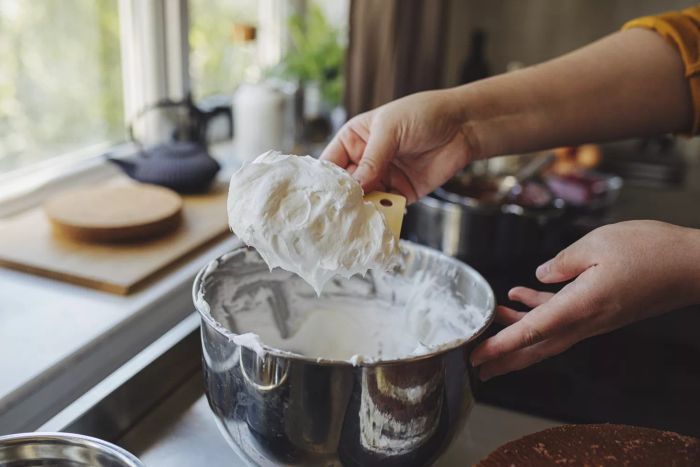 A close-up image of an unidentified young Caucasian woman preparing whipped cream on her home kitchen counter
