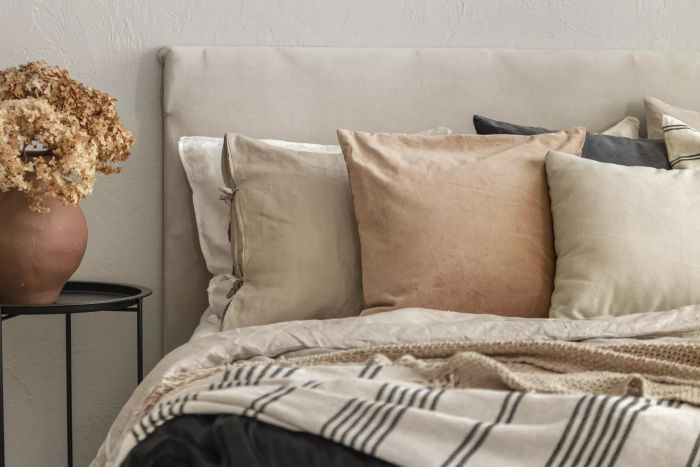 A brown flower arrangement in a ceramic vase on a metal nightstand next to a king-sized bed in a Scandinavian-style bedroom setting