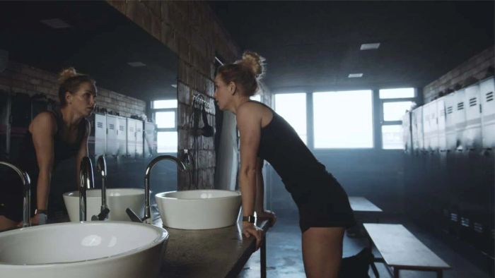 a woman in a gym locker room gazing into the mirror