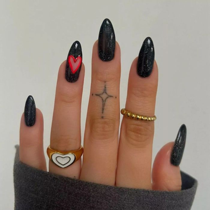 Sparkly black manicure with a heart on the ring finger outlined in red.