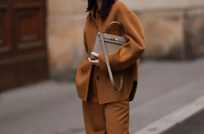 Leo Eberlin was spotted wearing a brown two-piece ensemble from Arket, featuring a jacket with a dark brown button placket, collar, and large chest pockets, paired with wide-legged trousers with a crease; a beige leather 'Kelly' bag from Hermès; and a diamond ring.