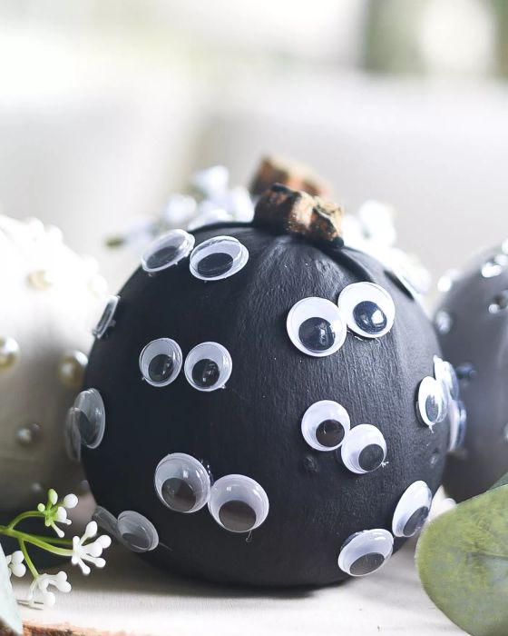 A black pumpkin adorned with pairs of googly eyes glued on it.
