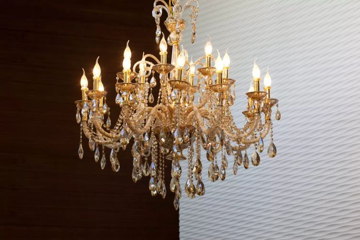 A lavish gold chandelier set against a black wooden backdrop, showcasing classic lighting design and interior decor
