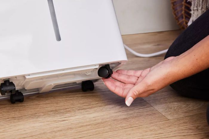 A hand adjusting a wheel on the underside of a tilted Homelabs 8-Pint Dehumidifier