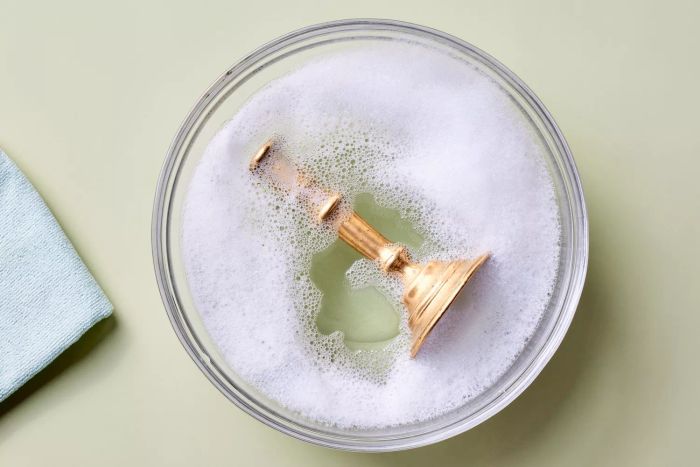 A brass candlestick being cleaned in a soapy bath