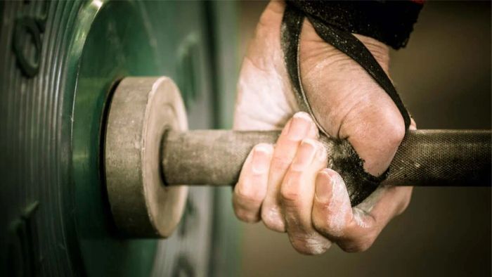 An individual demonstrates the hook grip on a barbell, with thumb tape securely wrapped around their thumbs.