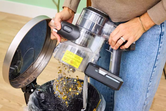 A person disposing of dirt from the Tineco Pure One S11 Vacuum into a trash can