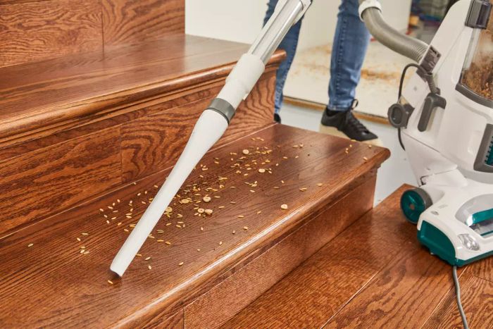 A person is vacuuming a spill on wooden stairs with the Shark NV501 Rotator Professional Lift-Away Upright Vacuum.