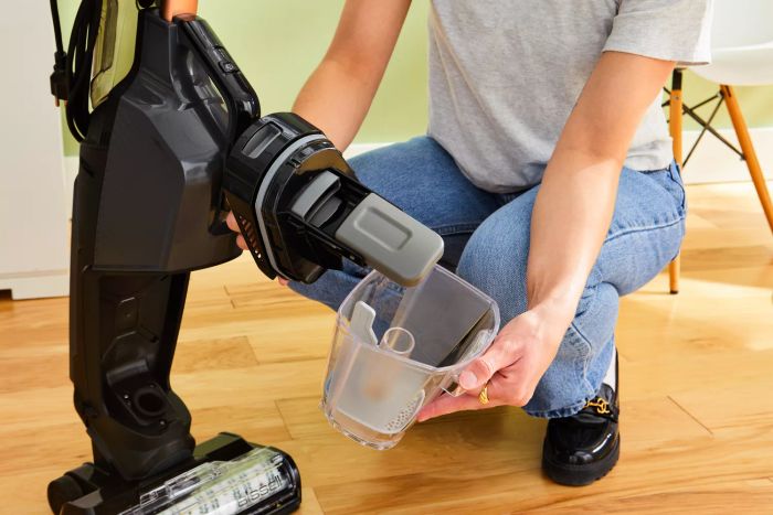 A person is emptying the container from the Bissell CrossWave HydroSteam Plus Multi-Surface Wet Dry Vac.