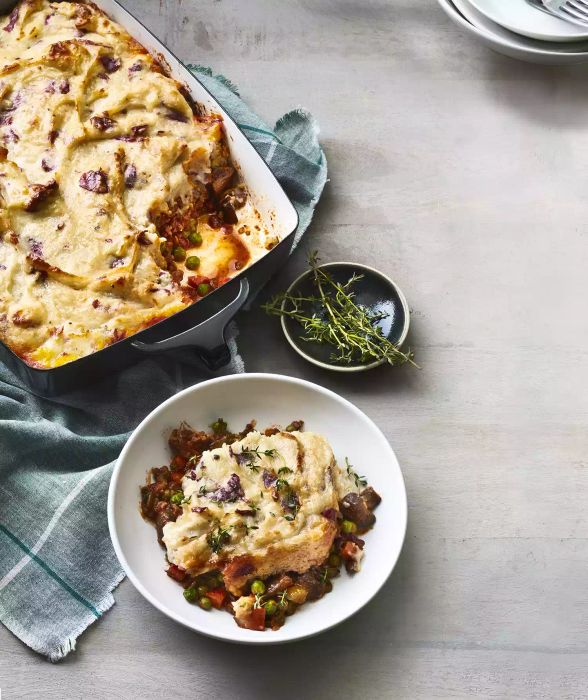 Simple Shepherd's Pie in a baking dish placed on a blue kitchen towel, served in a small white bowl with fresh thyme sprigs on a small black dish