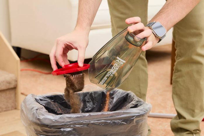 An individual disposing of debris from a Dirt Devil Versa 3-in-1 Cordless Stick Vacuum Cleaner into a trash bin.