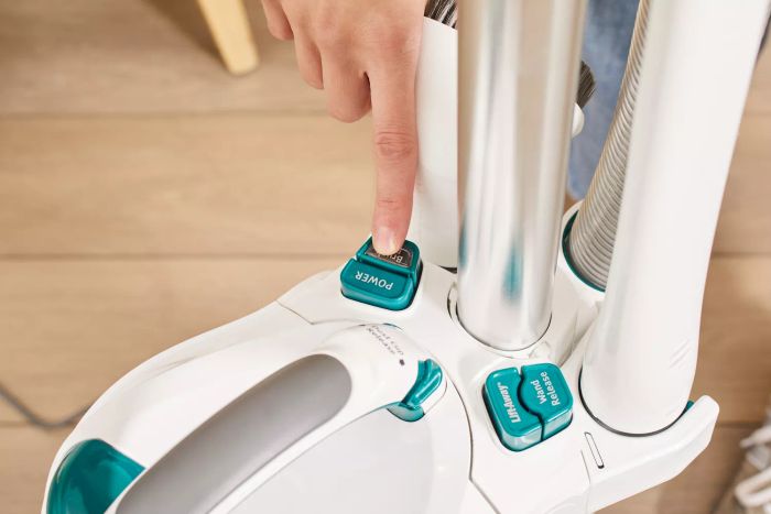 A person is pressing the power button on the Shark NV501 Rotator Professional Lift-Away Upright Vacuum.