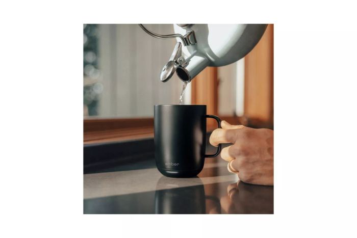A person pouring water from a tea kettle into the Ember Mug 2