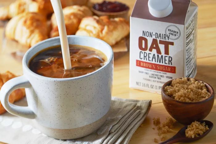 A photo of Trader Joe's Non-Dairy Oat Creamer Brown Sugar Flavor alongside a cup of coffee
