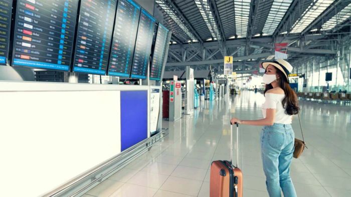 A masked traveler is seen at the airport, observing the arrival and departure screens.