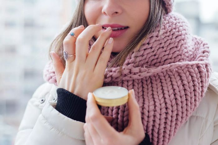 A person wearing a pink knitted scarf and applying lip balm to their lips with their fingers