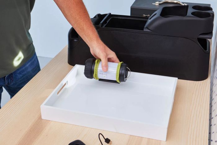 A person placing the Lighting Ever 3300019 Rechargeable LED Camping Lantern into a white tray.