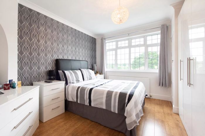 A wide-angle shot of a bedroom featuring black and white striped bedding paired with minimalist white furniture