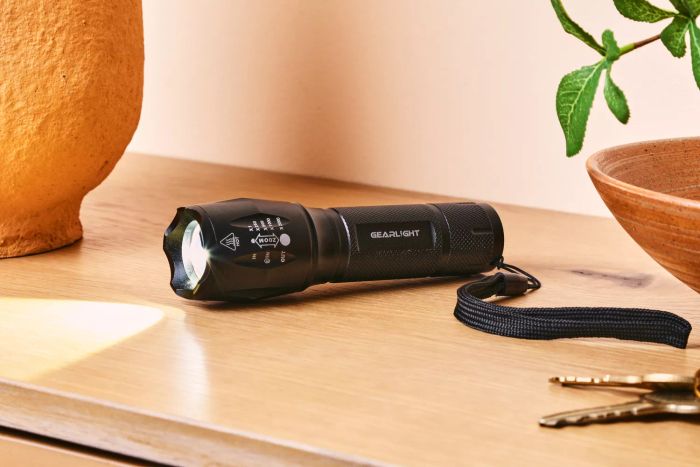A GearLight S100 LED Tactical Flashlight powered on, placed on a wooden countertop.