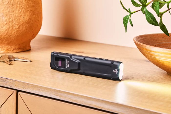 A lit Nitecore EDC27 Ultra Slim Flashlight resting on a wooden countertop.