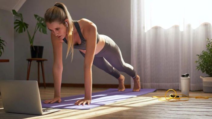A woman cautiously glances at her laptop while performing a workout
