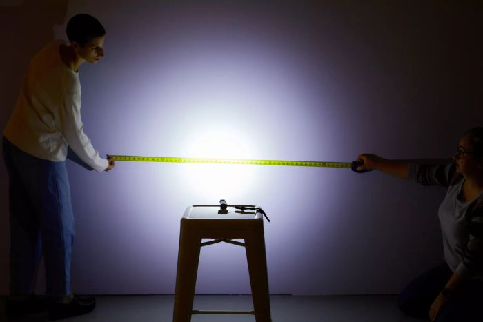 Individuals using the Olight S2R Baton II USB Magnetic Rechargeable Flashlight to measure its beam length on a wall