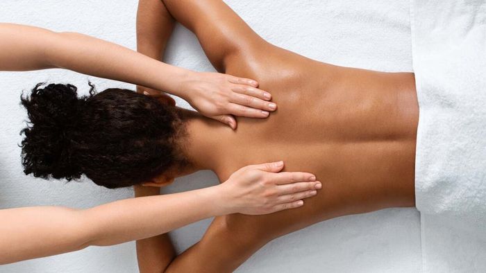 A woman rests on her stomach while a therapist performs a massage
