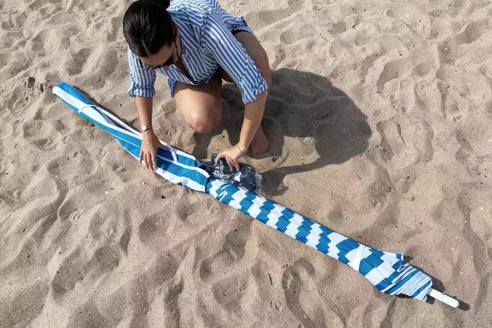 A person unpacking the OutdoorMaster Beach Umbrella with Sand Bag and Cup Holder
