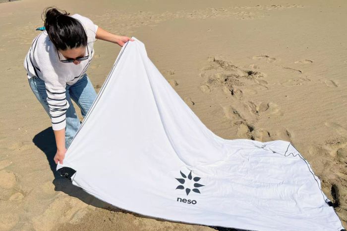 A person sets up the Neso 1 Beach Tent on the beach sand.