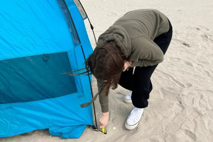 A person setting up the Pacific Breeze Easy Setup Beach Tent by the shore