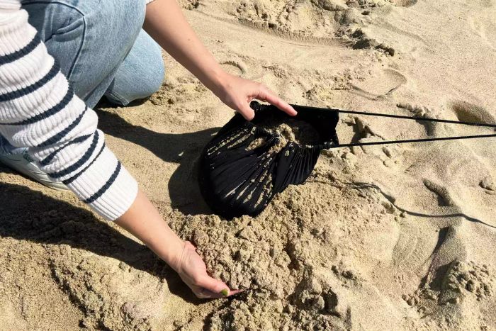 A person filling the sandbag for the Neso 1 Beach Tent with sand.