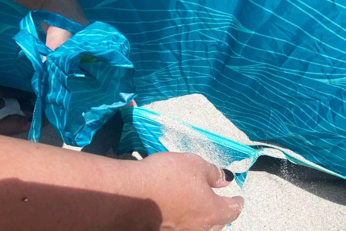 A close-up of hands filling the sand pocket of the Lightspeed Outdoors Quick Cabana Beach Tent with sand.
