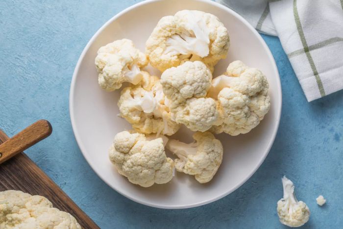 Freshly sliced cauliflower florets in a light bowl, placed on a blue backdrop with ample space for text.