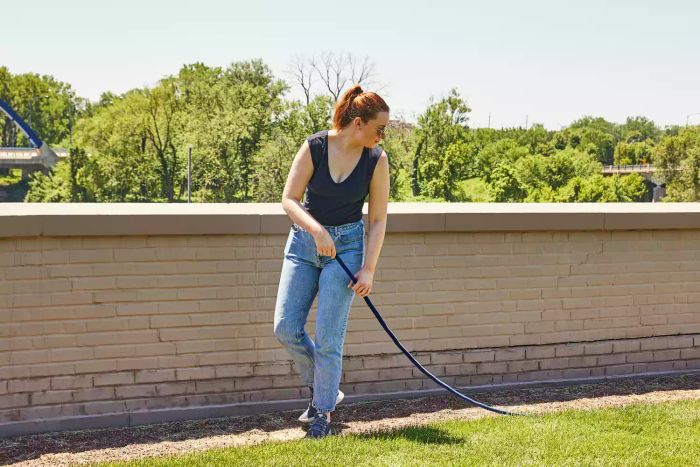 Person pulling the TheFitLife Flexible and Expandable Garden Hose across the grass.