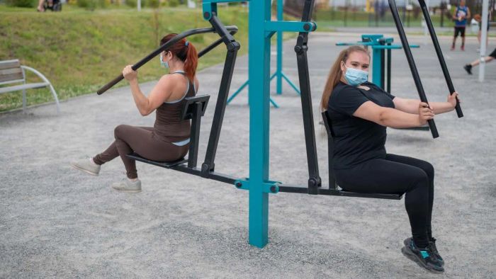A group of friends in masks are using outdoor gym equipment, and one of them appears...frustrated.