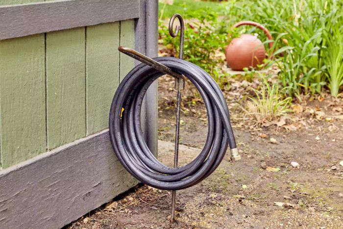 Coiled Briggs and Stratton Heavy-Duty Rubber Garden Hose displayed on a stand in a garden beside a house.
