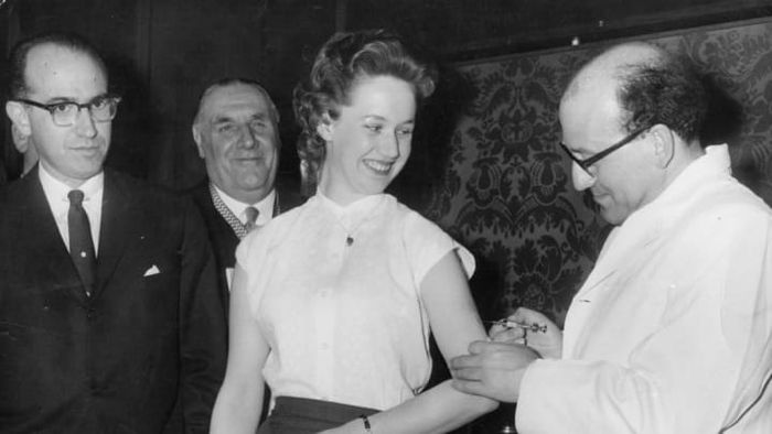 Jonas Salk, the American physician and epidemiologist who created the first polio vaccine, watches as a colleague administers the shot to a woman.
