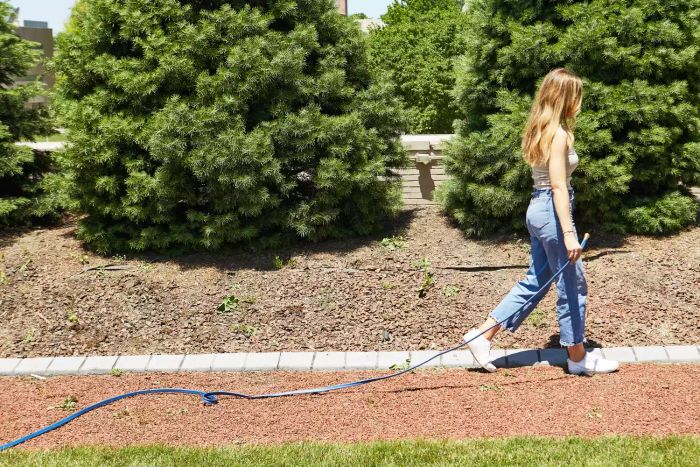 A person dragging the H2O Works Garden Flat Soaker Hose across a grassy area.