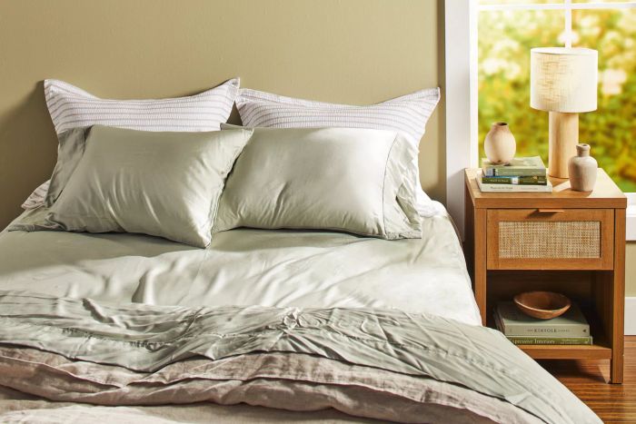 The Bamboo Bay 4-Piece Bamboo Sheet Set elegantly arranged on a bed with cushions, positioned beside a nightstand.
