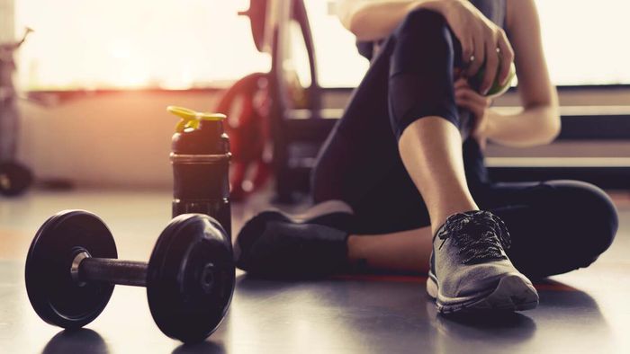 A resting athlete in running shoes sits beside a dumbbell, symbolizing the balance between cardio and strength.
