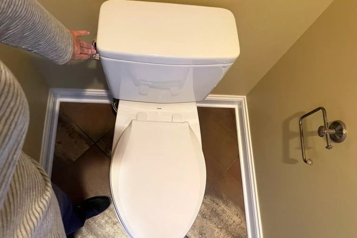 An individual engaging the flush mechanism of the Toto Drake Two-Piece Elongated Toilet